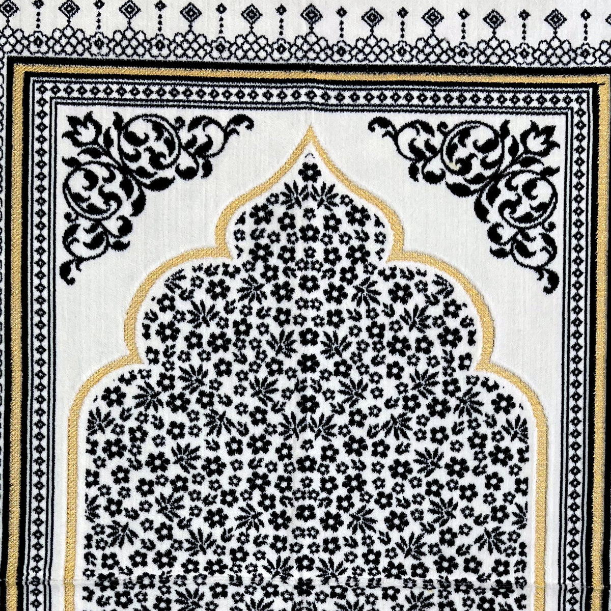 Close view of the dark blue mat — the gold-outlined arch, the dense floral field inside it and the scrolled corner medallion, showing the short woven pile.