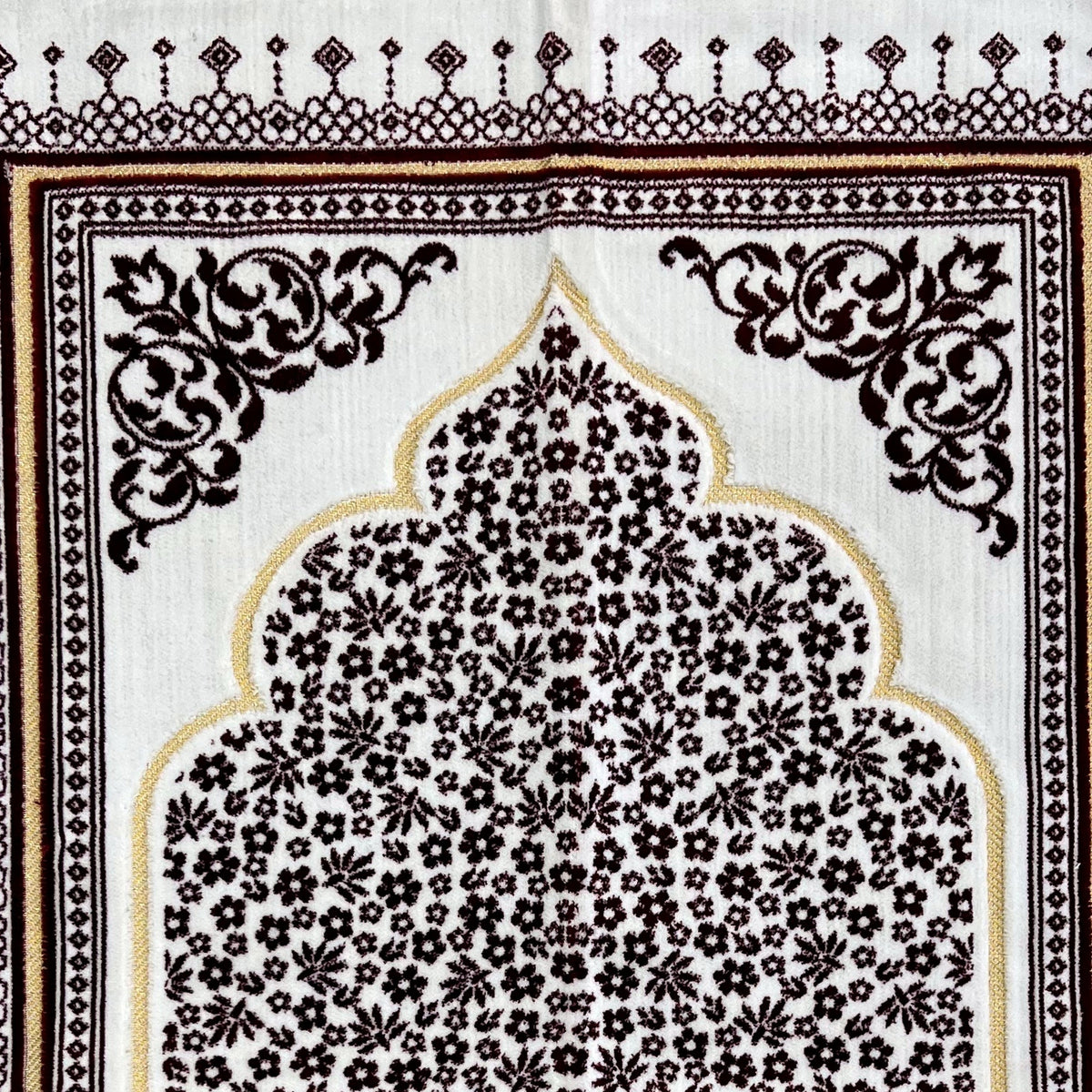 Close view of the dark red mat — the gold-outlined arch, the dense floral field inside it and the scrolled corner medallion, showing the short woven pile.