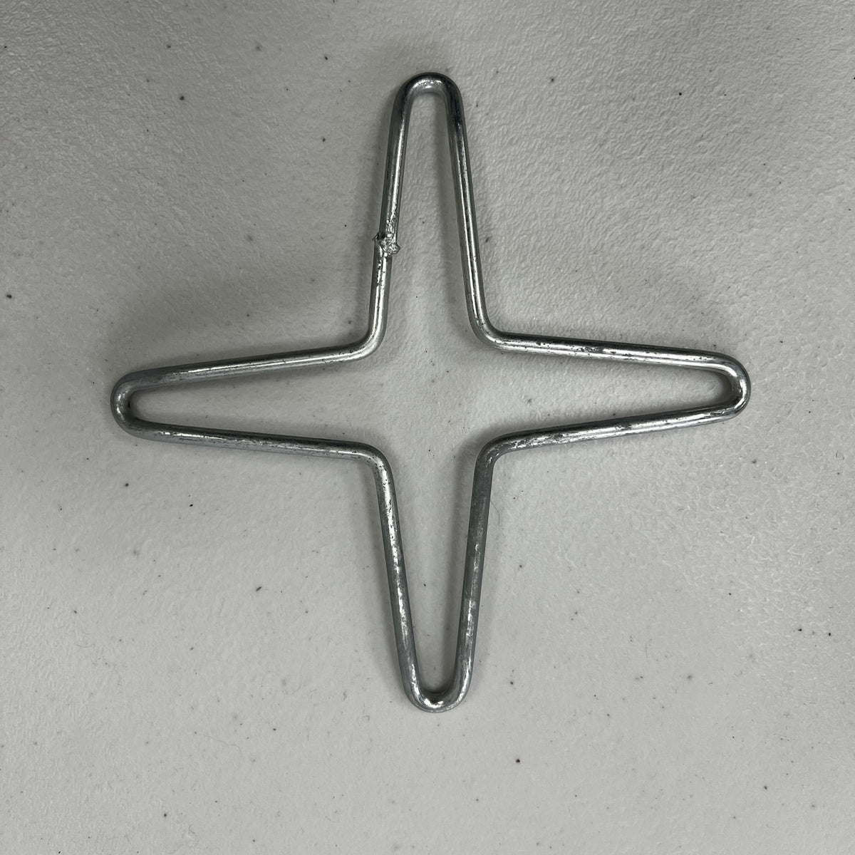 Galvanized steel wire stove trivet shaped as a 4-point star on a grey surface